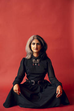 payal kumar sits in a black dress with a red background