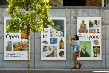 A man holding a bouquet of flowers passes by large banners promoting the Harvard Art Museums.