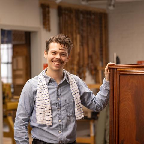 Artist stands next to a wooden furniture piece