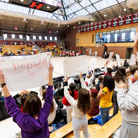 kids In the auditorium stands in the gymnasium cheering on the basketball team holding up signs