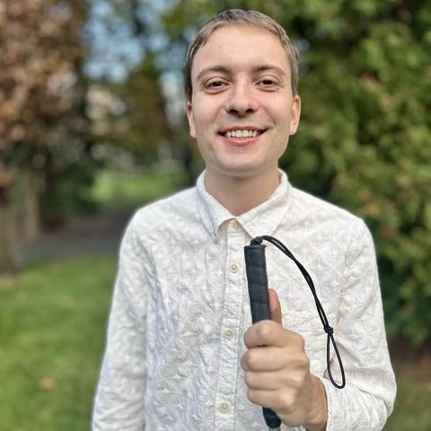 man poses for picture outdoors holding a blindness cane