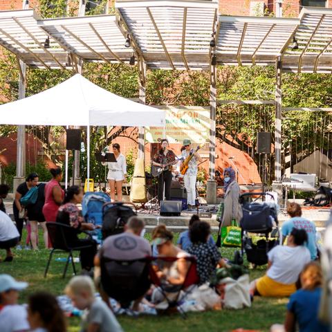 People sitting outside in courtyard watching a musical band 