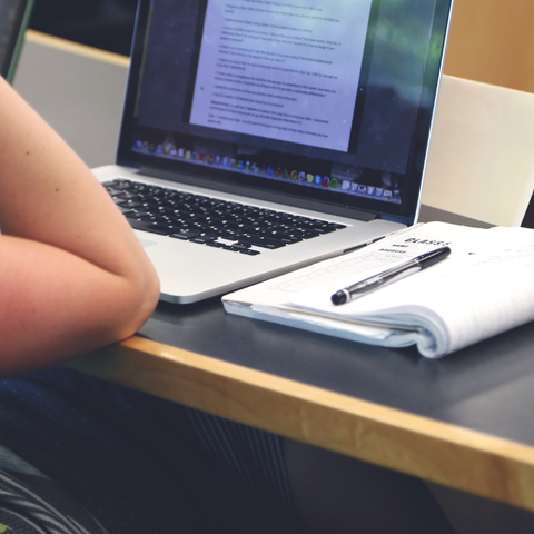 woman leaning on table in class with notes and laptop