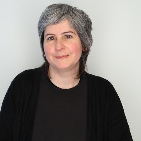 Artist jennifer purins posing for headshot wearing black, half smiling, with white background