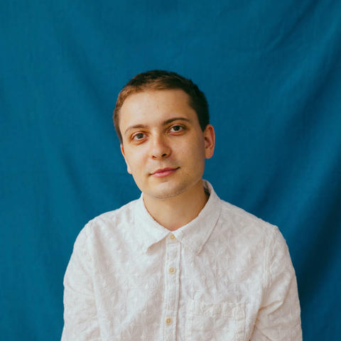 Man sits to pose for photo wearing white shirt with blue background