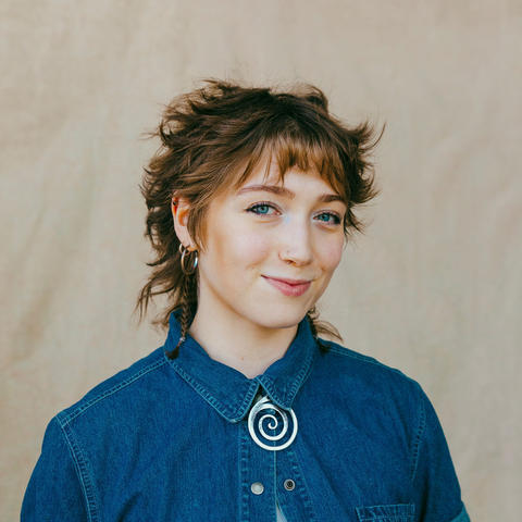woman wearing blue denim button up poses in front of beige background