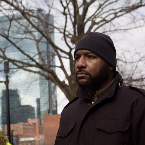 man wearing coat and beanie stands outside in front of boston Prudential building