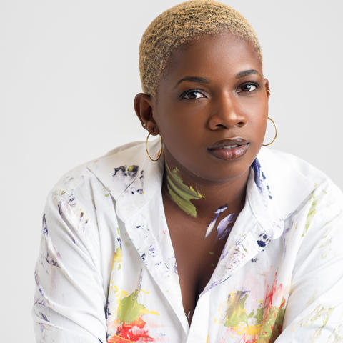 woman in paint spotted white button up shirt sits for headshot