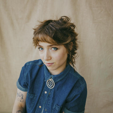 woman sits in jean jacket with a beige sheet background