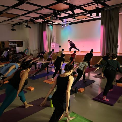 people standing in yoga pose, instructor on stage, pink uplights