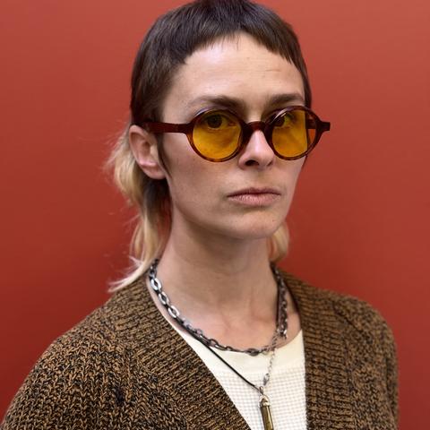Headshot of Kate Audet wearing sunglasses standing in front of red wall