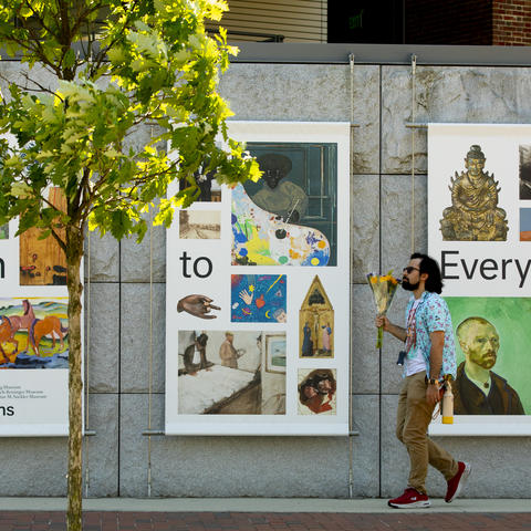 A man holding a bouquet of flowers passes by large banners promoting the Harvard Art Museums.