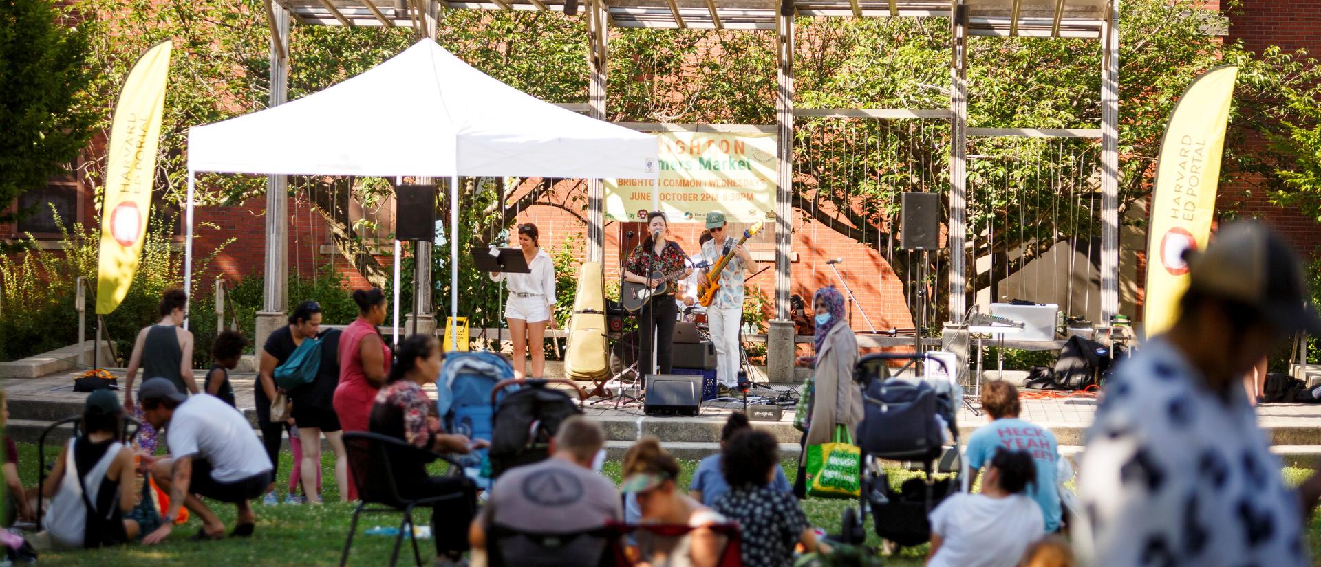 People sitting outside in courtyard watching a musical band 