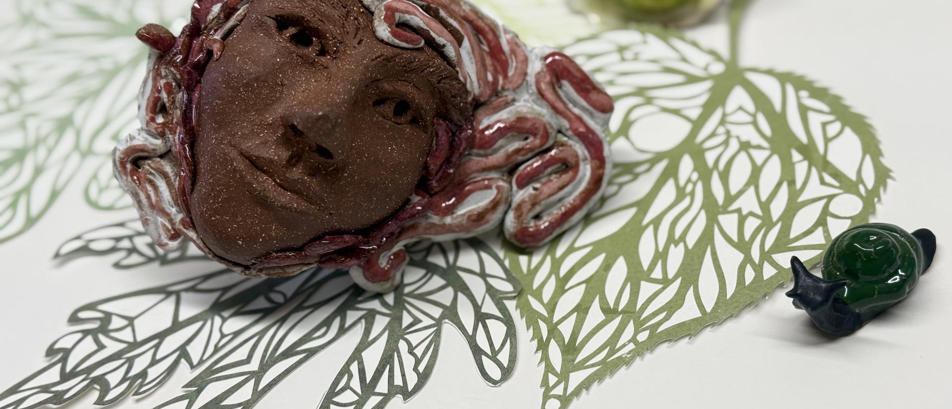 leaf prints on white paper with brown sculpture of a face by artist tashi haig