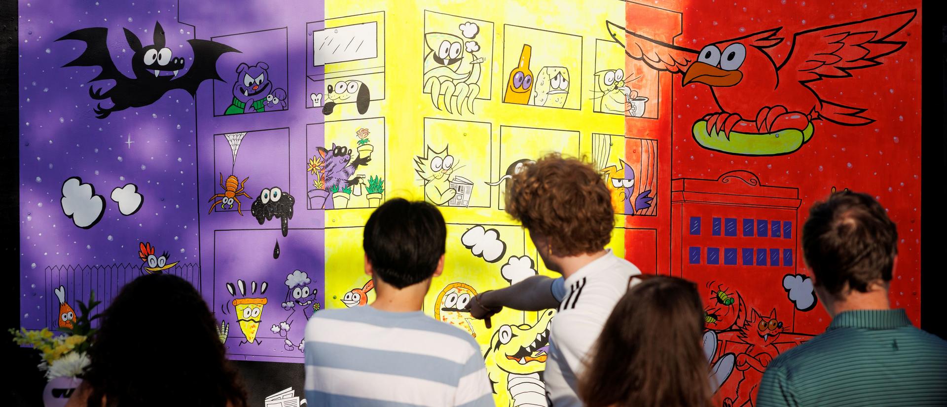 People standing in front of a mural pointing out different characters